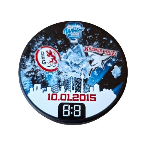 DEL Winter Game 2015 DEG Kölner Haie Eishockeypuck Sammlerstück Sammlungsauflösung Draufsicht auf den originalen DEL Winter Game Event Puck vom zehnten Januar zweitausendfünfzehn mit den Logos der DEG und Kölner Haie sowie der Skyline von Düsseldorf.
