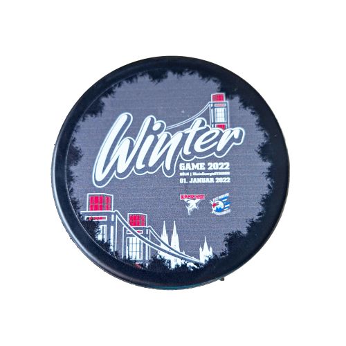 Offizieller Eishockey-Puck des DEL Winter Game 2022 im Kölner RheinEnergieSTADION. Der Puck ist schwarz und zeigt das Event-Logo mit dem Schriftzug „Winter Game 2022“, dem Spieldatum „01. Januar 2022“ sowie den Logos der Kölner Haie und Adler Mannheim vor einer Stadion-Silhouette.
