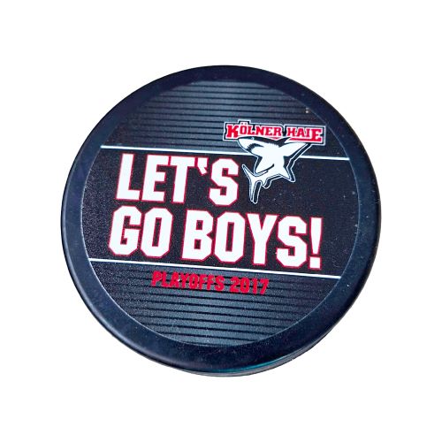 Offizieller Eishockey-Puck der Kölner Haie aus den Playoffs 2017. Der Puck ist schwarz und zeigt das Kölner Haie Logo, den weißen und roten Schriftzug „Let's Go Boys! Playoffs 2017“ auf einem gemusterten, dunklen Hintergrund.
